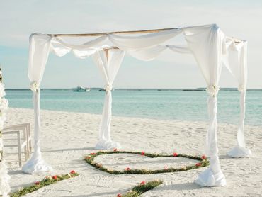 White canopy and floral heart arrangement set the scene for a romantic beachfront wedding ceremony.