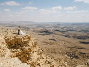 Adventurous couple poses on a cliff edge after an epic elopement in the desert with panoramic views.