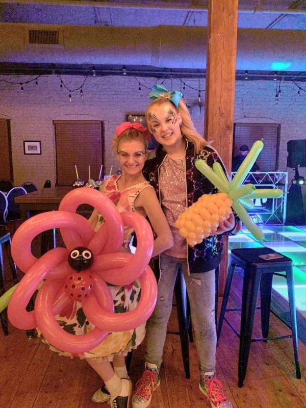 Two girls holding balloon sculptures, one flower and one pineapple.