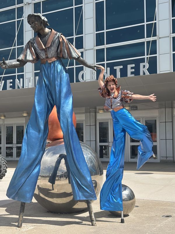 Person and sculpture on stilts in blue pants outside a center.