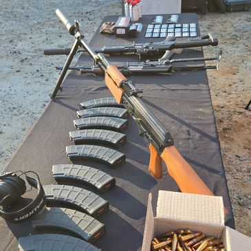 Assorted firearms and ammunition displayed on a table outdoors.