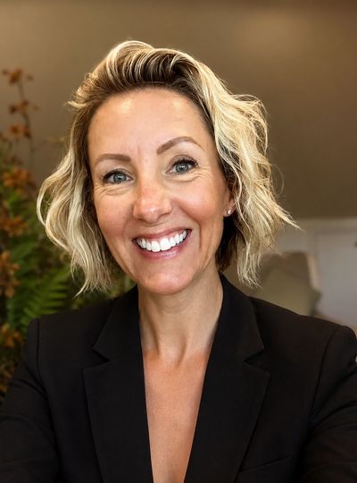 Smiling woman with short blonde hair wearing a black blazer.