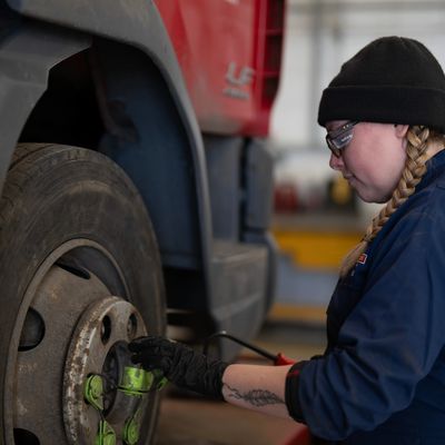 A mechanic working on a truck's wheel lug nuts in a garage.