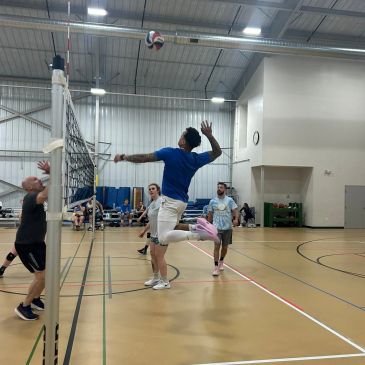 Men playing volleyball indoors, one jumping to hit the ball.