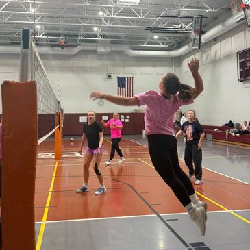 Girls playing volleyball indoors in a gymnasium.