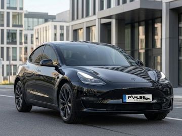 Black Tesla Model 3 parked in front of modern buildings.