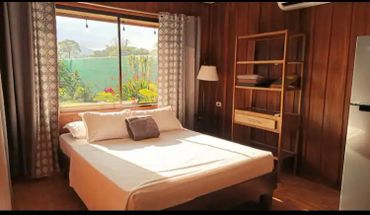 Cozy bedroom with wooden walls and large window overlooking garden.