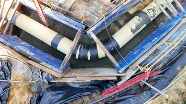 Construction site with large pipes installed in a trench and supported by blue braces.