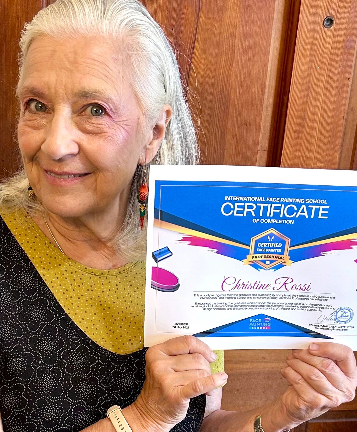 Elderly woman proudly holding a face painting certificate.