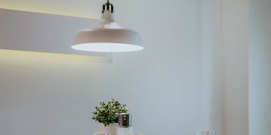 Minimalist white kitchen pendant light illuminating a small plant on a counter.