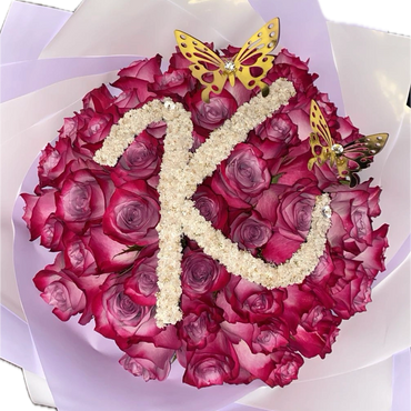 Bouquet of pink roses decorated with a white floral letter K and golden butterflies.