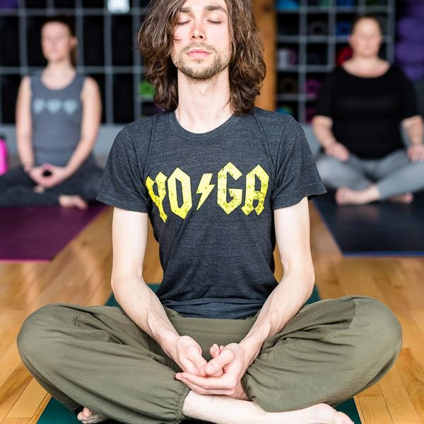 attractive young man with long hair meditating on yoga mat in yoga studio. 