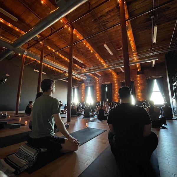 students seated on mats in a yoga class inside yoga studio meditating. 
