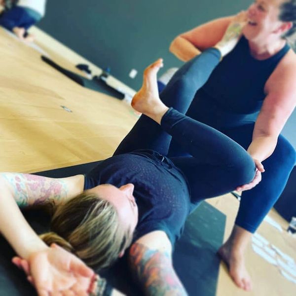 yoga teacher assisting hands on a student in a yoga posture inside yoga studio