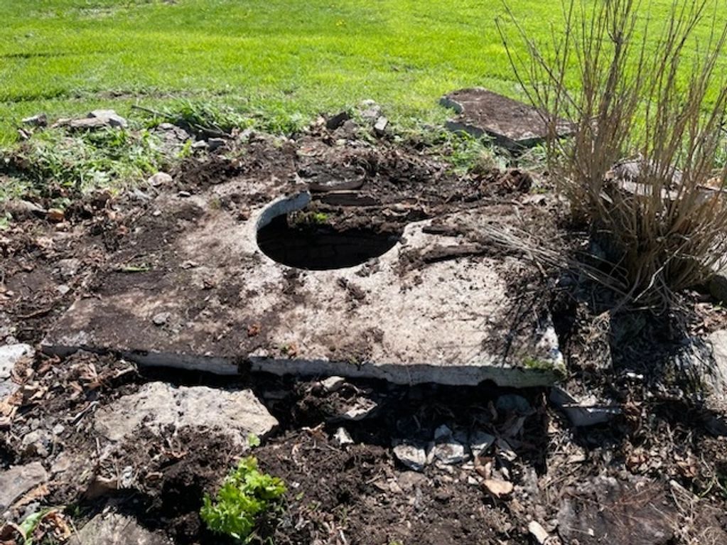 Old stone slab with a circular hole in a garden area.
