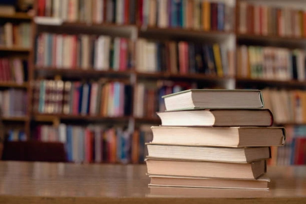 Stack of books on a table in a library with blurred shelves in the background.