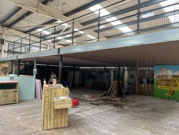 Indoor construction site with wooden structures and scaffolding under unfinished ceiling.