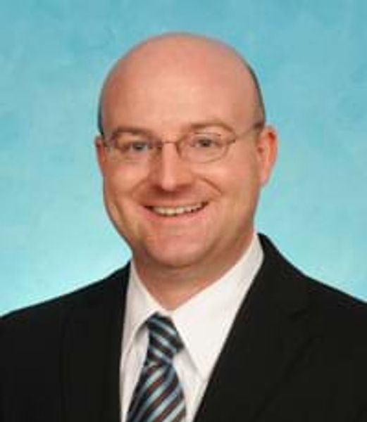 Smiling bald man in glasses wearing a suit and striped tie.