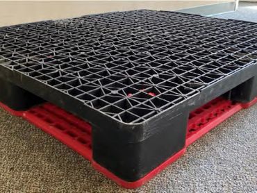 Black plastic pallet with red base on carpet.