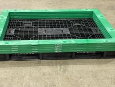 Stacked plastic pallets with green frames on a warehouse floor.