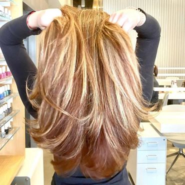 Person showing their long, highlighted hair from the back in a salon.