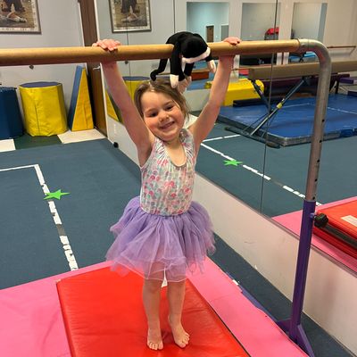 Little girl in a tutu holding a gymnastics bar and smiling.
