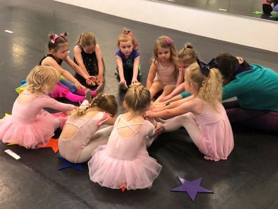 Young ballerinas in pink tutus stretch in a circle during dance class.