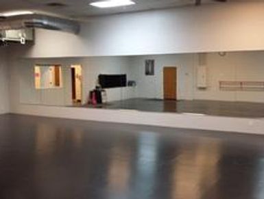 Empty dance studio with mirrored wall and wooden floor.