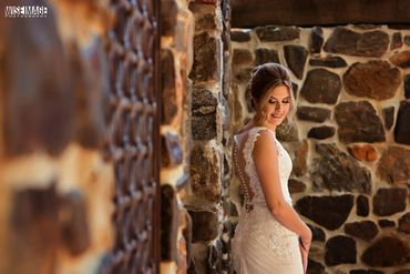Elegant bride in a lace wedding dress standing by a rustic stone wall.