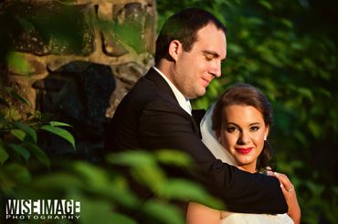 A groom tenderly embraces his bride outdoors, surrounded by greenery.