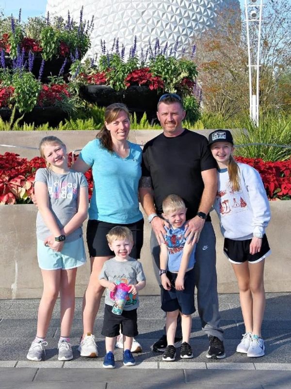 A family of six posing happily at a theme park with colorful flowers and a large spherical structure behind them.