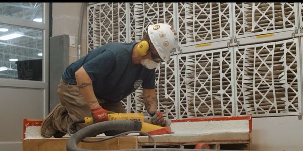 Construction worker using a power tool indoors with safety gear.