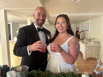 Newlywed couple smiling and holding drinks at reception.