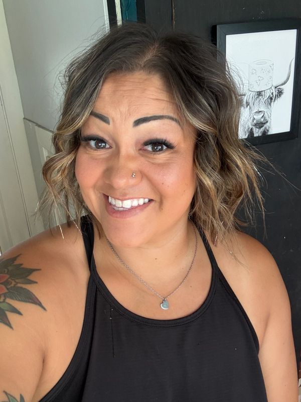 Smiling woman with curly hair and tattoo wearing a black tank top.