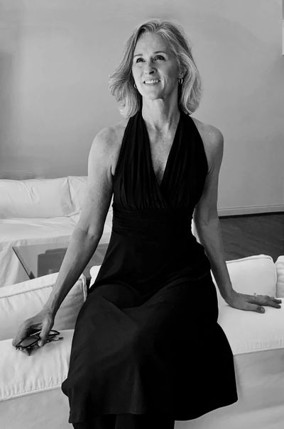 Elegant woman in a black dress sitting on a white couch, smiling.