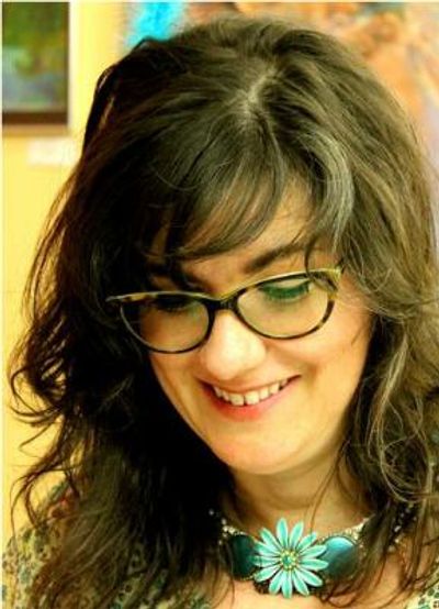 Artist Jeanne Burris Johnson in an art studio, smiling with wavy dark hair, glasses