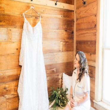 A woman admiring a white wedding dress hanging on a wooden wall.