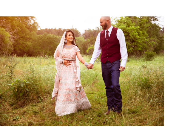 A newlywed couple holds hands and smiles in a sunlit meadow.