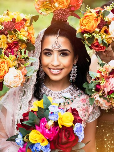 Smiling bride adorned with jewelry and vibrant flower bouquets.