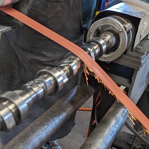Camshaft being polished with sparks flying off.