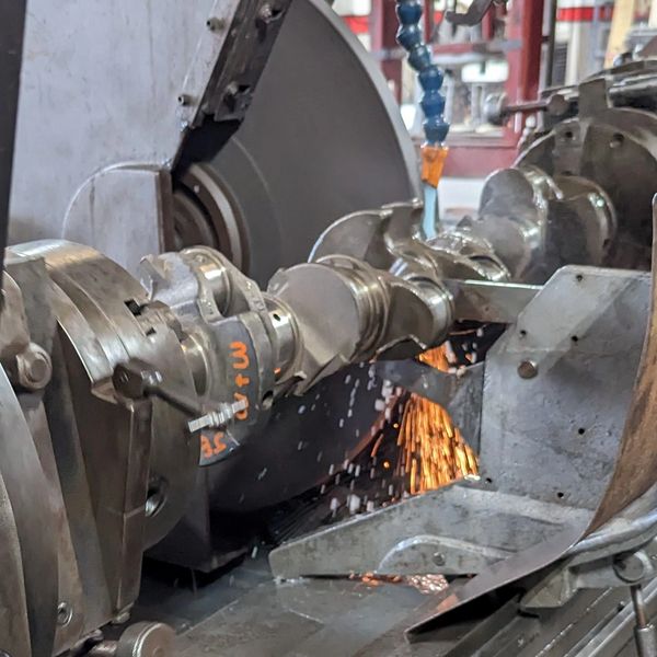 Industrial grinding machine grinding a crankshaft with sparks flying.