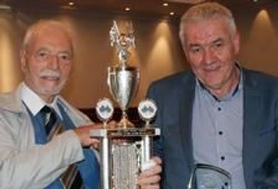 Two elderly men holding trophies.