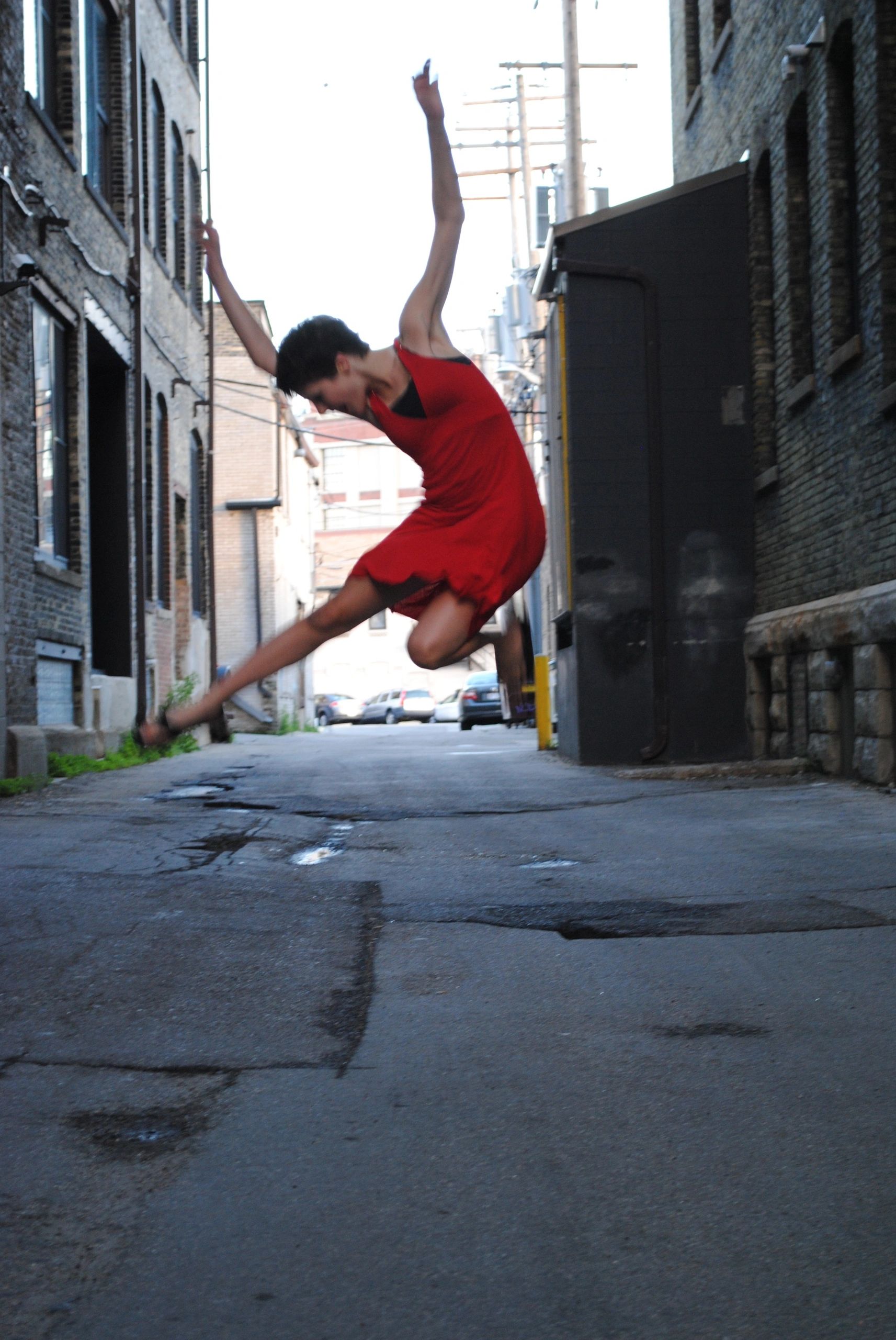 Young woman in red dress jumping in an alley between two buildings