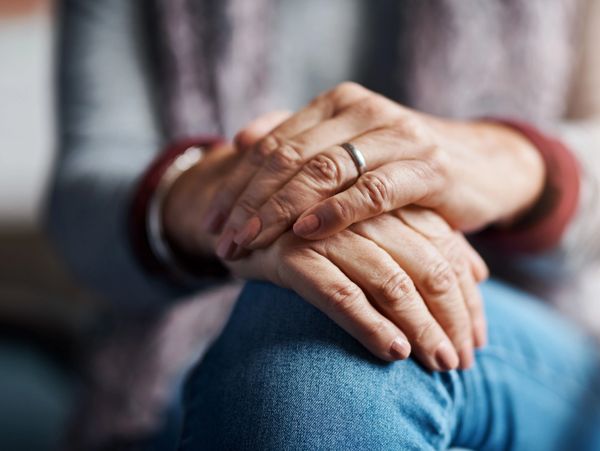 An older adult person is sitting with both hands crossed on their own knee.