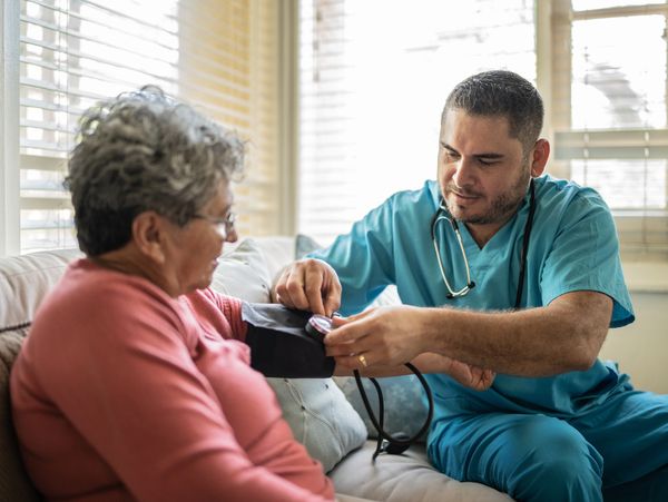 A young man healthcare professional sitting next to an elderly woman, taking her blood pressure.