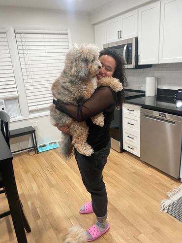 pet sitter standing in kitchen carrying large fluffy bernedoodle