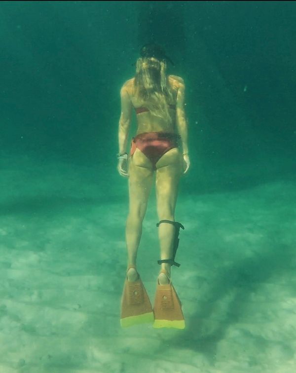 Woman snorkeling underwater wearing fins and a red bikini.