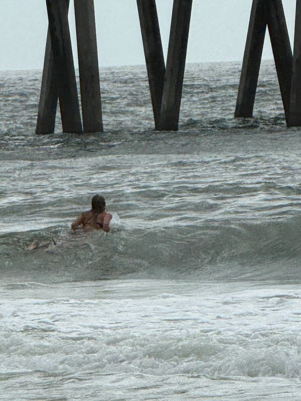 Person swimming in the ocean near pier pillars.
