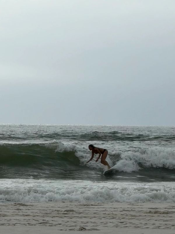 A woman surfing a wave near the beach on a cloudy day.
