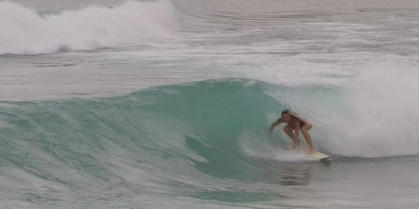 Surfer crouching inside a breaking turquoise wave.